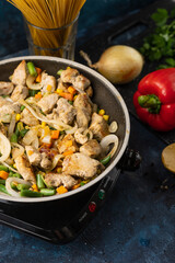 Macro shot top view of pan with fragrant frying meat and mix of vegetables on the stove near ingredients on dark blue background. Backstage of cooking pasta. Traditional italian cuisine. Food concept.