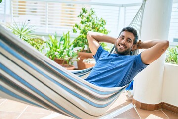 Young hispanic man relaxed smiling happy lying on the hammock at terrace.