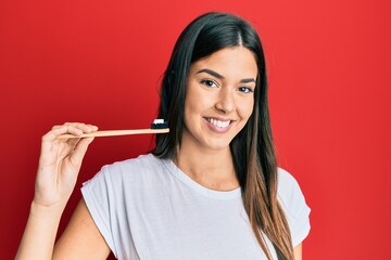 Young brunette woman holding toothbrush with toothpaste looking positive and happy standing and smiling with a confident smile showing teeth