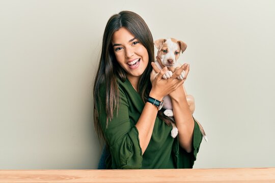 Young hispanic girl smiling happy and hugging dog sitting on the table over isolated white background.