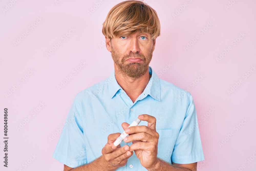 Sticker Young blond man using glucose meter depressed and worry for distress, crying angry and afraid. sad expression.