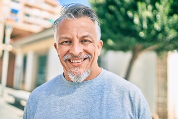 Middle age hispanic grey-haired man smiling happy standing at the city.