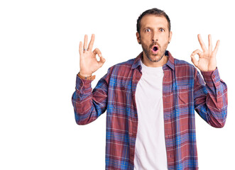 Young handsome man wearing casual clothes looking surprised and shocked doing ok approval symbol with fingers. crazy expression