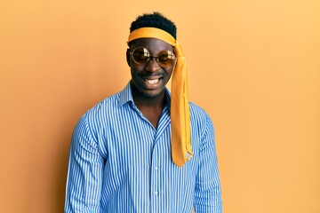 Handsome black man drunk wearing tie over head and sunglasses winking looking at the camera with sexy expression, cheerful and happy face.