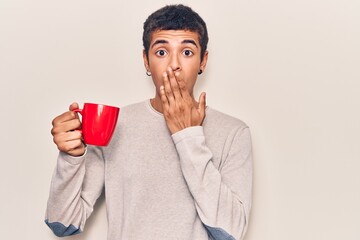 Young african amercian man holding coffee covering mouth with hand, shocked and afraid for mistake....