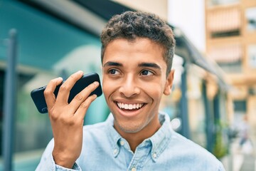 Young latin man smiling happy listening audio message using smartphone at the city.