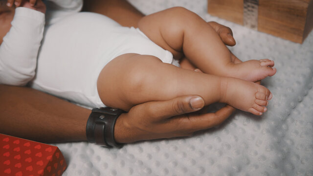Close up, dad holding cute baby feet surrounded by christmas gifts. Multiracial family. High quality photo