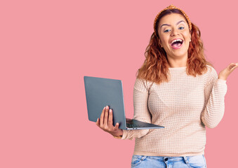 Young latin woman holding laptop celebrating victory with happy smile and winner expression with raised hands