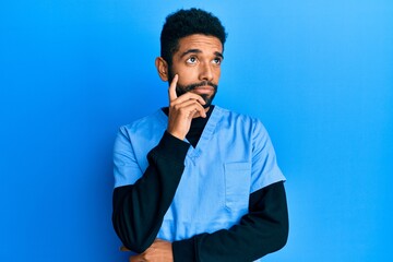 Handsome hispanic man with beard wearing blue male nurse uniform serious face thinking about...