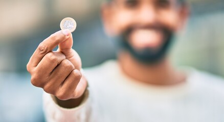 Young african american man smiling happy showing 1 euro coin at the city.