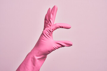 Hand of caucasian young man with cleaning glove over isolated pink background picking and taking invisible thing, holding object with fingers showing space