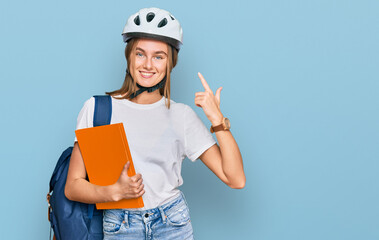 Beautiful young blonde woman wearing backpack and bike helmet smiling happy pointing with hand and finger