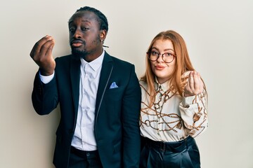 Young interracial couple wearing business and elegant clothes doing italian gesture with hand and fingers confident expression