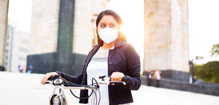 Business woman with mask, she is standing and has a bicycle. Carry a green bag - Powered by Adobe