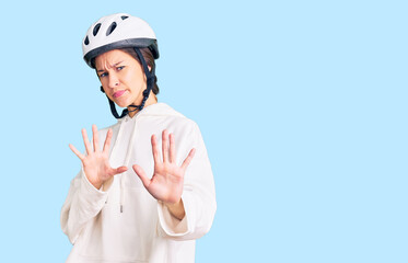 Beautiful brunette young woman wearing bike helmet and sporty clothes disgusted expression, displeased and fearful doing disgust face because aversion reaction. with hands raised
