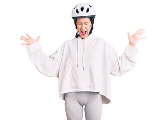 Beautiful brunette young woman wearing bike helmet and sporty clothes celebrating mad and crazy for success with arms raised and closed eyes screaming excited. winner concept