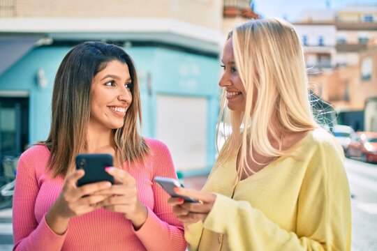 Two beautiful and young girl friends together having fun at the city using smartphone