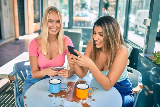 Two beautiful and young girl friends together at cafeteria using smartphone