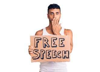 Young hispanic man holding free speech banner covering mouth with hand, shocked and afraid for...