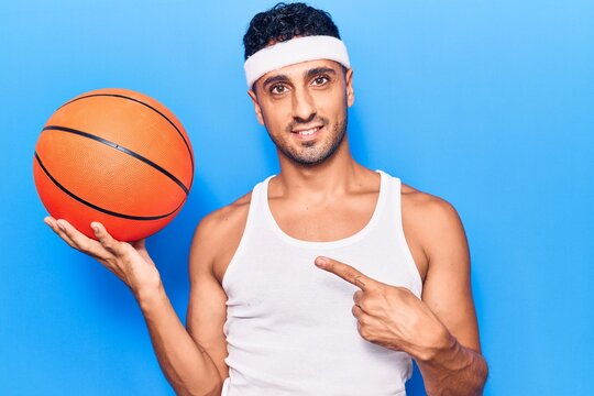 Young hispanic man holding basketball ball smiling happy pointing with hand and finger