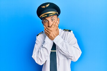 Handsome man with beard wearing airplane pilot uniform shocked covering mouth with hands for mistake. secret concept.