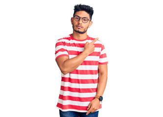 Handsome latin american young man wearing casual clothes and glasses pointing with hand finger to the side showing advertisement, serious and calm face