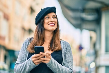 Young latin woman wearing french style using smartphone at the city.