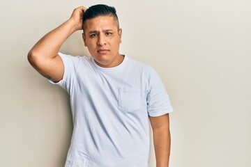 Young latin man wearing casual white t shirt confuse and wonder about question. uncertain with...