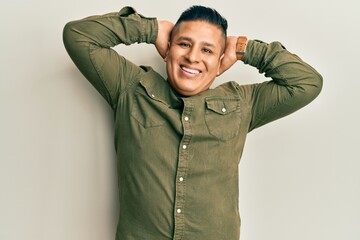 Young latin man wearing casual clothes relaxing and stretching, arms and hands behind head and neck smiling happy