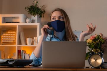 Young woman working in office in protective mask and uses phone. Concept of coronavirus pandemic in the world.