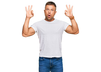 Handsome muscle man wearing casual white tshirt looking surprised and shocked doing ok approval symbol with fingers. crazy expression