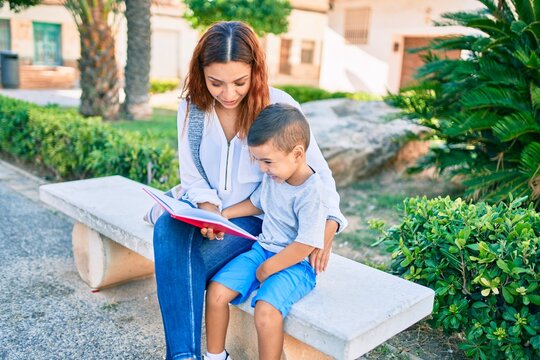 Adorable latin mother and son sitting on the bench and reading book at the park.