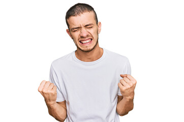 Fototapeta premium Hispanic young man wearing casual white t shirt very happy and excited doing winner gesture with arms raised, smiling and screaming for success. celebration concept.