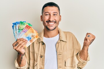 Handsome man with tattoos holding swiss franc banknotes screaming proud, celebrating victory and...