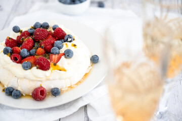 Pavlova with strawberries, raspberries, blueberries and passionfruit and sparkling wine in the foreground