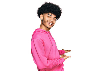 Young african american man with afro hair wearing casual pink sweatshirt inviting to enter smiling natural with open hand