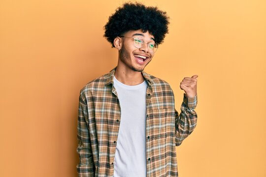 Young african american man with afro hair wearing casual clothes pointing thumb up to the side smiling happy with open mouth