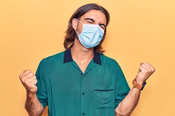 Young handsome man wearing medical mask very happy and excited doing winner gesture with arms raised, smiling and screaming for success. celebration concept.