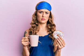 Young blonde girl wearing sleep mask and pyjama having breakfast skeptic and nervous, frowning...