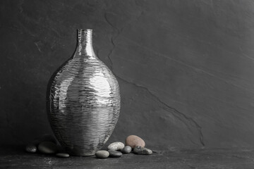 Stylish silver ceramic vase and rocks on black table, space for text