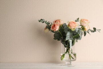 Vase with bouquet of beautiful roses on white wooden table. Space for text