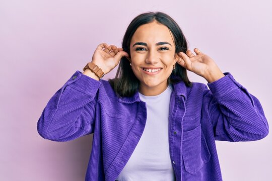 Young brunette woman wearing casual clothes smiling pulling ears with fingers, funny gesture. audition problem