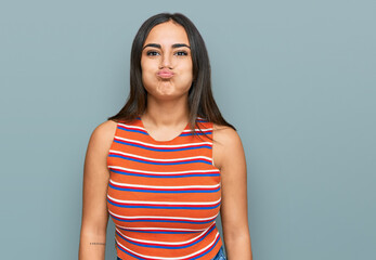 Obraz premium Young brunette woman wearing casual clothes puffing cheeks with funny face. mouth inflated with air, crazy expression.