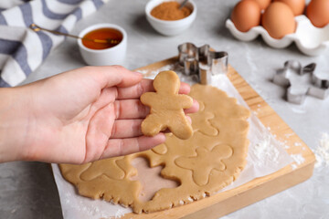 Making homemade Christmas cookies. Woman holding gingerbread man above light grey marble table, closeup