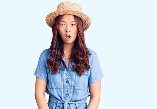 Young beautiful chinese girl wearing summer hat afraid and shocked with surprise and amazed expression, fear and excited face.