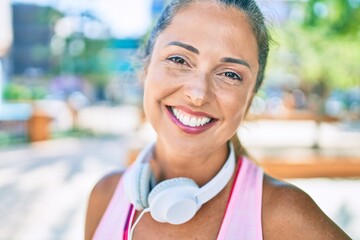 Middle age sportswoman smiling happy  wearing headphones at the park