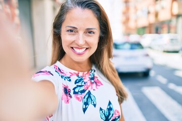 Young hispanic woman smiling happy making selfie by the camera at city