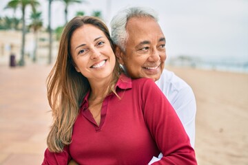 Obraz premium Middle age hispanic couple smiling happy and hugging sitting on the bench.