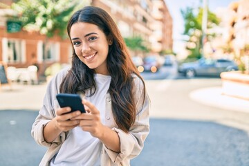 Fototapeta na wymiar Young hispanic woman smiling happy using smartphone at the city.