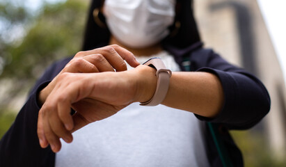 Close-up of Latin businesswoman wearing a face mask for protective reasons during the covid 19 pandemic. She is checking the time on her watch